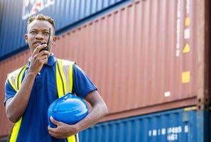 Adult African american men worker Check and control loading freight Containers by use radio at commercial shipping dock feeling curious. Cargo freight ship for import export concept photo