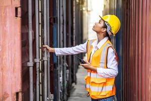 joven ingeniera segura de sí misma que usa comunicación por radio y usa casco de seguridad amarillo y verifica la caja de contenedores de carga de control del buque de carga para importación y exportación foto