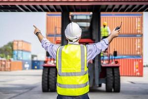 Rear view of engineer in reflective clothing with safety helmet is working and checking at containers cargo on shipping port area at harbor photo