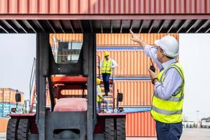 joven ingeniero o gerente que usa la comunicación por radio para controlar la carga de contenedores en la industria frente al contenedor de elevación de máquinas y el espacio de carga. conceptos de transporte y logística. foto