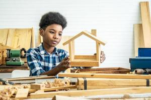 African-American boy carpenter looks at his own wooden house that helps his father happily do it photo