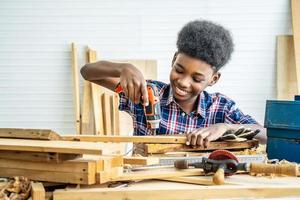 retrato de un niño afroamericano que usa camisa con un taladro en las manos y ayuda a papá a armar un estante de muebles con una herramienta de destornillador eléctrico, concepto de aprendizaje.