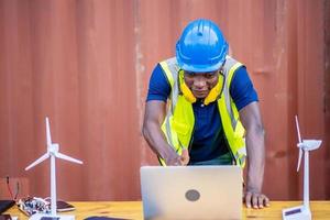 A male engineer using laptop, making video call to client or business partner by the negotiations were successful., On desk are windmill models. Sustainable development concept photo