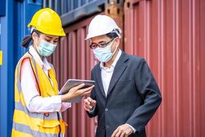 Industrial worker woman and engineer control worker using tablet device and meeting in front of container and cargo. Business people with confident and smart working in shipping transport industry photo