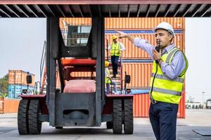 joven ingeniero o gerente que usa la comunicación por radio para controlar la carga de contenedores en la industria frente al contenedor de elevación de máquinas y el espacio de carga. conceptos de transporte y logística. foto