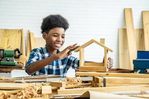 sonriente niño afroamericano carpintero feliz trabajando con madera y papel de lija foto