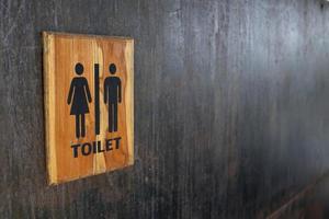 Toilet sign in wood frame on black painted metal wall. Some rusty and scratch on surface of wall. photo