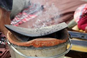 placa de arado de hierro negro sobre una olla de fuego de arcilla y fondo borroso, humo sobre la placa de arado. equipo de preparación para masaje tailandés al estilo norteño. foto