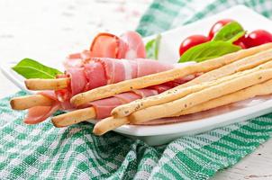 Grissini bread sticks with ham, tomato and basil photo