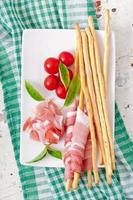 Grissini bread sticks with ham, tomato and basil photo