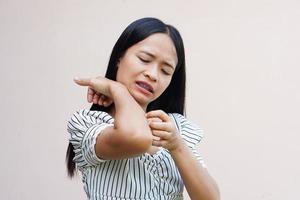 mujer rascándose el brazo por picazón en un fondo gris claro. la causa de la picazón en la piel incluye picaduras de insectos concepto de cuidado de la salud de la piel. foto