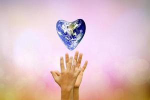 Earth conservation concept. The world of hearts floats above human hands. nature blur background photo