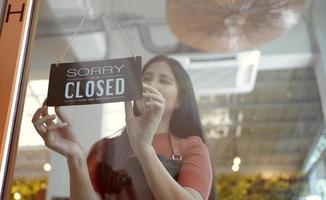 la mano de la mujer de la cafetería propietaria voltea el letrero para cerrar la tienda. letrero cerrado colgado en la puerta de vidrio. foto