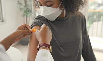 African american doctor is applying plaster to a child's shoulder after being vaccinated. Opening sleeves to vaccinate against flu or epidemic in health care and vaccinated concept.