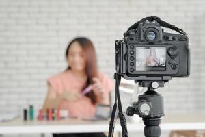 Asian young attractive woman beauty blogger happy talking and review cosmetic product while recording camera live stream online to audience from home. Selective focus. photo