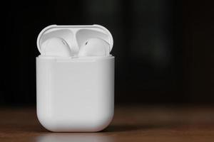 White color true wireless earphone in opened charging case ready for pairing on wooden table. Copy space. Selective focus. photo