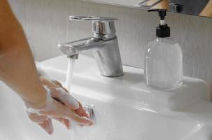 Asian man washing hands with soap in bathroom sink. Hygiene and COVID-19 prevention concept, copy space.