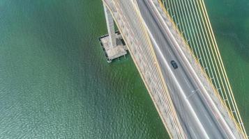 Aerial view of car driving on a bridge with natural forest trees, sand, tropical beach and waves rolling into the shore. photo