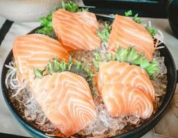 el sashimi consiste en un trozo de salmón crudo colocado sobre el hielo en una taza de cerámica negra en un restaurante. foto