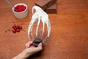 Metal whisk with whipped egg with shadows whites on wood table background photo