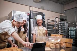 tres jóvenes socios de inicio de chefs, blogger de pequeñas empresas que transmiten en vivo a través de tecnología de aplicaciones móviles, promoción de ventas de panadería en línea, pan fresco, comida de pastelería y cocina comercial. foto