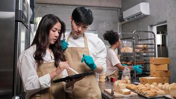 Three young friends and startup partners of bread dough and pastry foods busy with homemade baking jobs while cooking orders online, packing, and delivering on bakery shop, small business entrepreneur photo