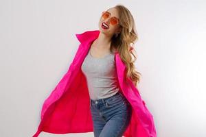Close up happy girl in red sunglasses and pink coat isolated on white background. excited, shock and surprised young woman, trendy outfit. Fashion and shopping concept. Long wavy hair. Selective focus photo