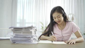 Woman with headphone taking notes on clipboard during a job video call while working from home.