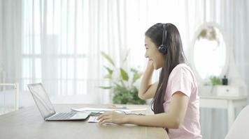 vrouw met koptelefoon die aantekeningen maakt op het klembord tijdens een videogesprek tijdens het werken vanuit huis.
