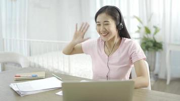 mujer con auriculares tomando notas en el portapapeles durante una videollamada de trabajo mientras trabaja desde casa. video