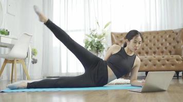 jeune femme sportive faisant des exercices d'étirement tout en regardant une vidéo de fitness en ligne sur un ordinateur portable à la maison. concept de mode de vie sain video