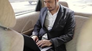 Businessman working on laptop computer in the seat of a car. A businessman is using a computer while riding in a car. Closeup of a male in formal wear with a laptop in a luxurious car. video