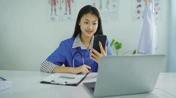 mooie vrouw arts zittend aan een bureau, met behulp van een smartphone, videobellen met patiënten online. in het kantoor van de kliniek op het werk video