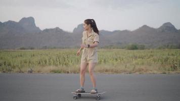 las mujeres asiáticas surfean en patineta en las calles fuera de la carretera rural con vistas a la montaña por la noche. concepto de estilo de vida. video