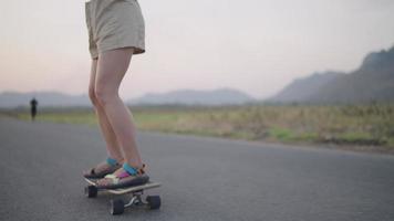 asiatische frauen surfen skateboarding auf den straßen außerhalb der landstraße mit blick auf die berge am abend. Lifestyle-Konzept. video