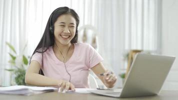 Woman with headphone taking notes on clipboard during a job video call while working from home.