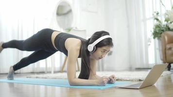 Sporty young woman doing stretching exercises while watching fitness video online on laptop at home. Healthy lifestyle concept