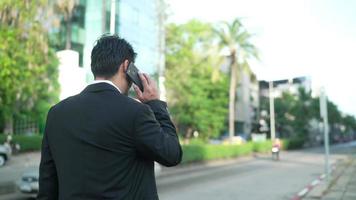 vista posteriore un uomo d'affari di successo stava camminando con un telefono in strada. uomo fiducioso che utilizza uno smartphone all'aperto. un uomo d'affari felice sta usando un telefono cellulare all'esterno. video