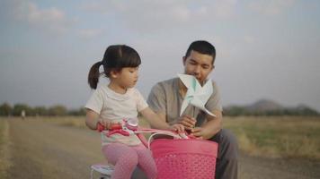 4k Video slow-motion, A father is teaching his daughter to learn to play with a turbine in the grass. Happily in the evening. Family concept.