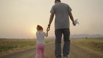 4k video slow-motion, een aziatische vader nam de hand van zijn dochter voor een wandeling. de rechterhand houdt een turbine vast tijdens het concept van de zonsondergangfamilie.