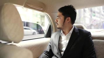 Slow-motion of a young, handsome businessman looking outside the window of his car during traveling in a modern car with a driver in the center of the city by video