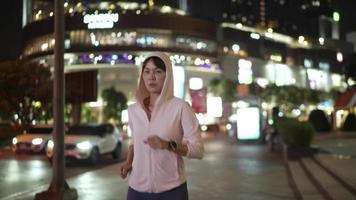 ralenti, police suivre la vue de la caméra. athlète féminine en chemise à capuche faisant du jogging dans les rues de la ville de nuit avec beaucoup de lumières en arrière-plan. video