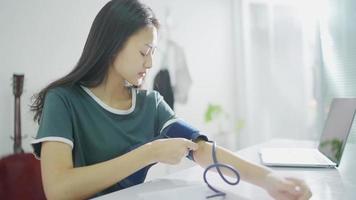 autocontrol de la mujer asiática, análisis, control de la presión arterial. equipos de salud, dispositivos en el hogar. mujer tailandesa mide la presión arterial en el dispositivo de reloj bp en el dormitorio en casa. video