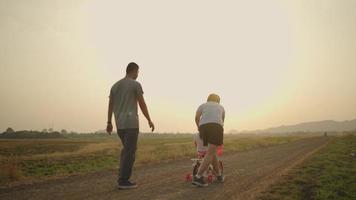 pai e mãe asiáticos levando sua filha bicicleta rosa no prado durante o pôr do sol. conceito de família.
