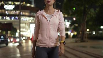 athlète féminine portant un sweat à capuche rose. pratiquer le jogging la nuit tous les jours. rues de la ville avec beaucoup de lumières en arrière-plan. concept de jogging nocturne urbain. video