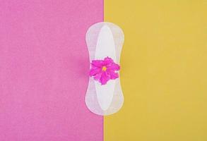 Sanitary pad for critical days and a purple flower on a pink-yellow background. Care of hygiene during menstruation. Regular menstrual cycle. Top view, copy space photo