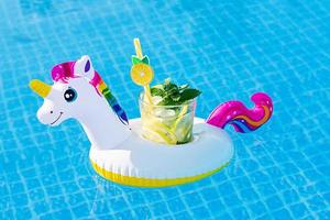 Fresh coctail mojito on inflatable white unicorn toy at swimming pool. Vacation concept.