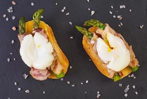 Grilled toast with asparagus in bacon and poached egg on wooden background photo