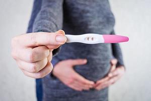 Young pregnant woman and her husband holding swollen belly with pregnancy test in her hand. photo