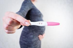 Young pregnant woman with swollen belly holding a pregnancy test photo